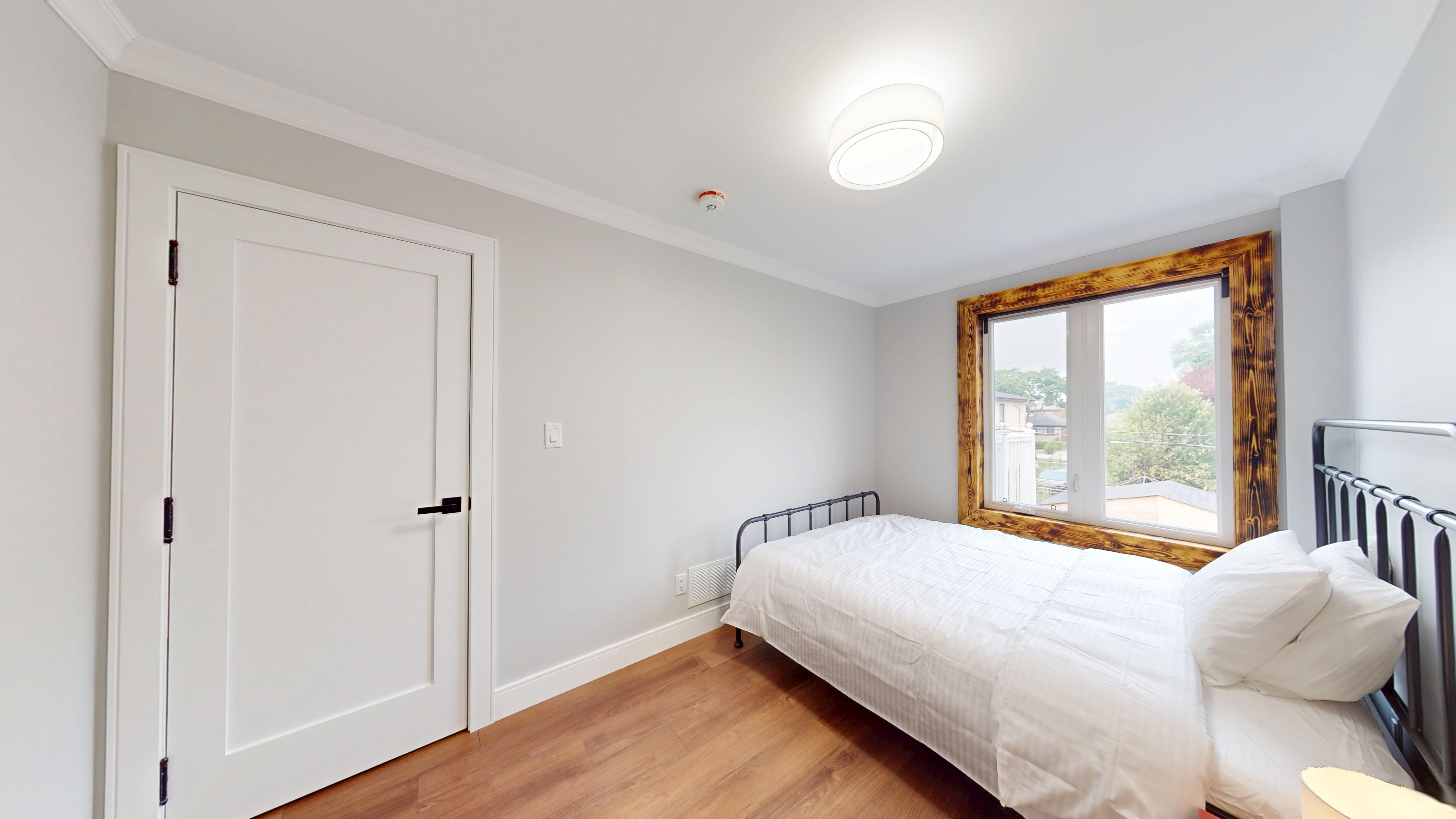 Bedroom 2: a bed beneath a burnt-wood framed window, with a closet by the door