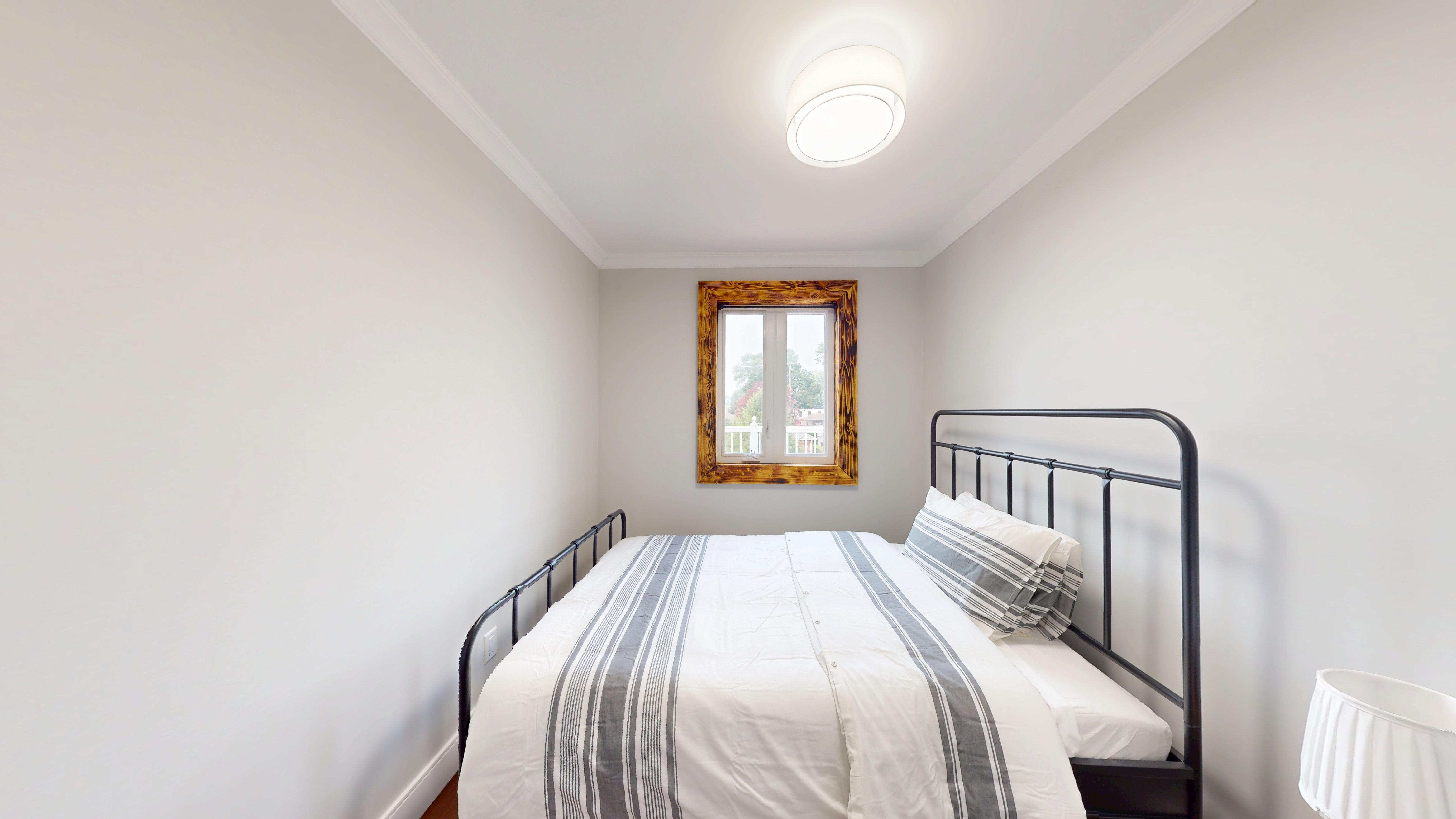 Bedroom 1: a bed in grey-striped linens beside a burnt-wood framed window