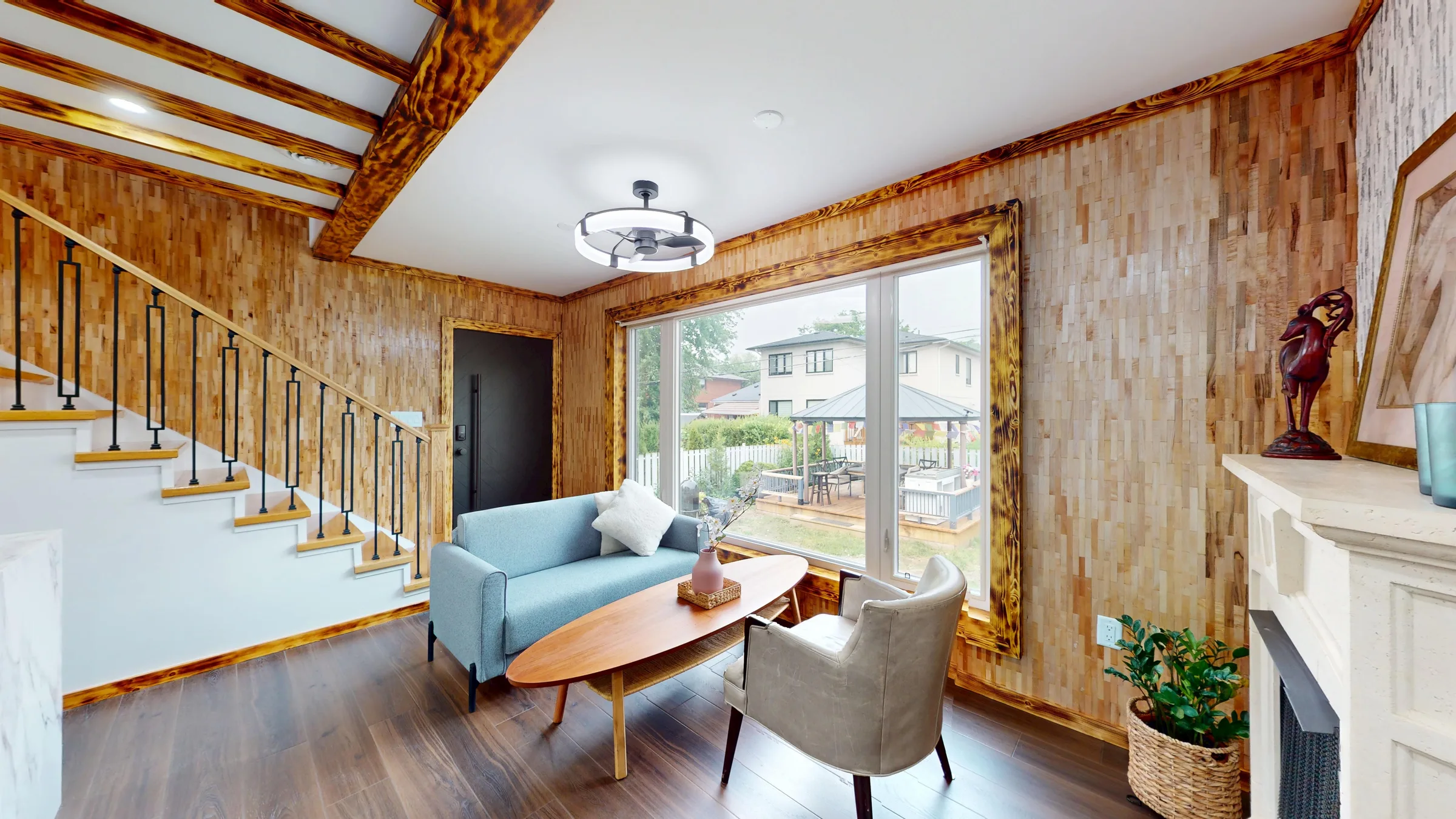 Living room with wood-tile accent walls, exposed beams and a view to the backyard deck