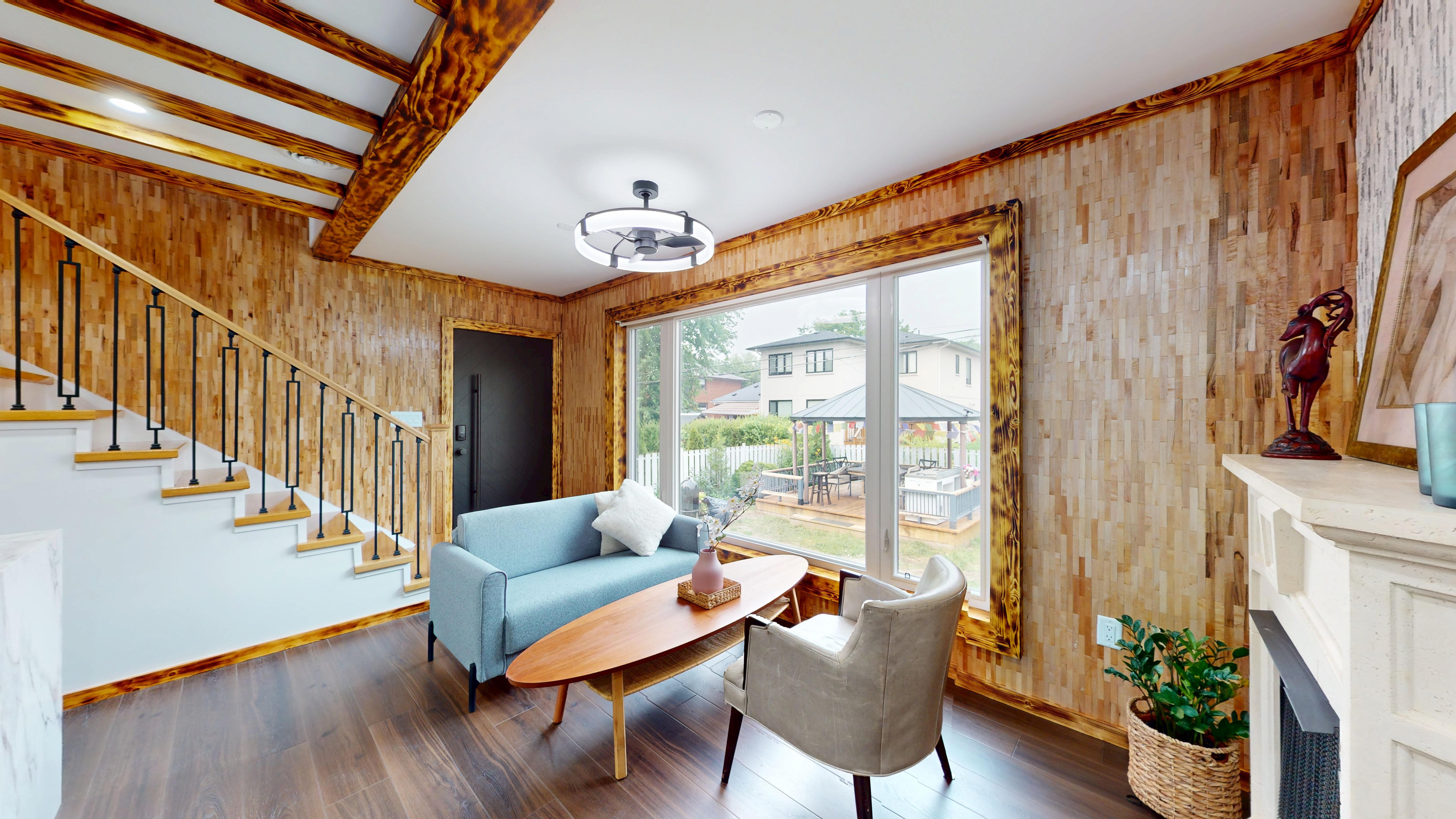 Living room with wood-tile accent walls, exposed beams and a view to the backyard deck