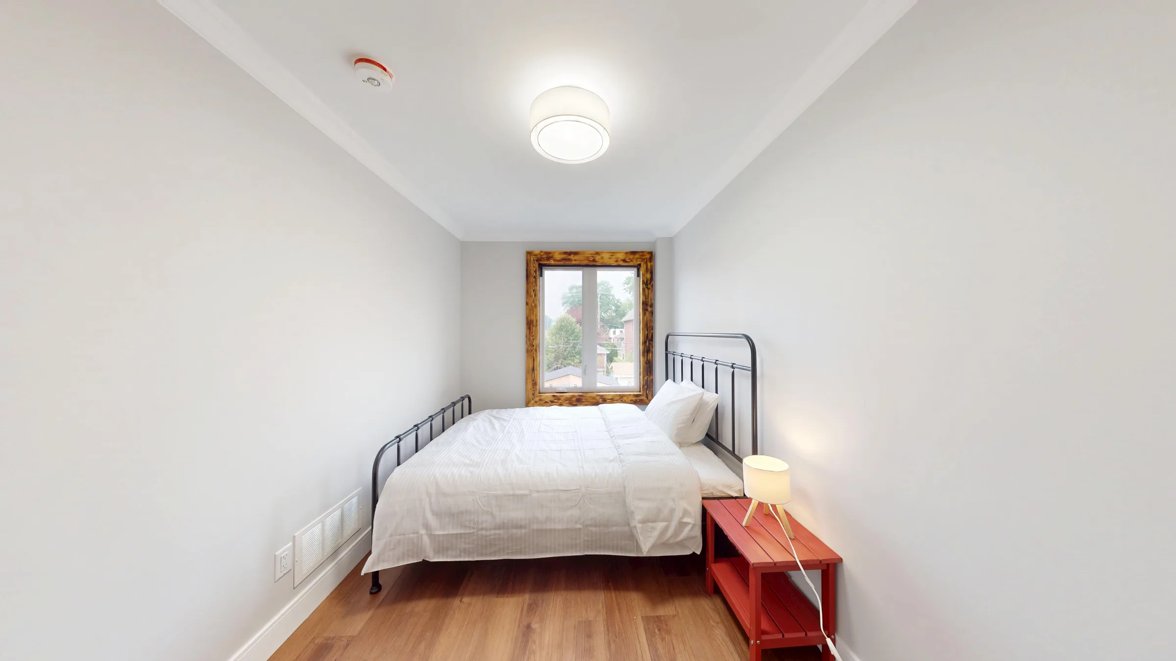 Bedroom with a red bedside bench beneath a burnt-wood framed window