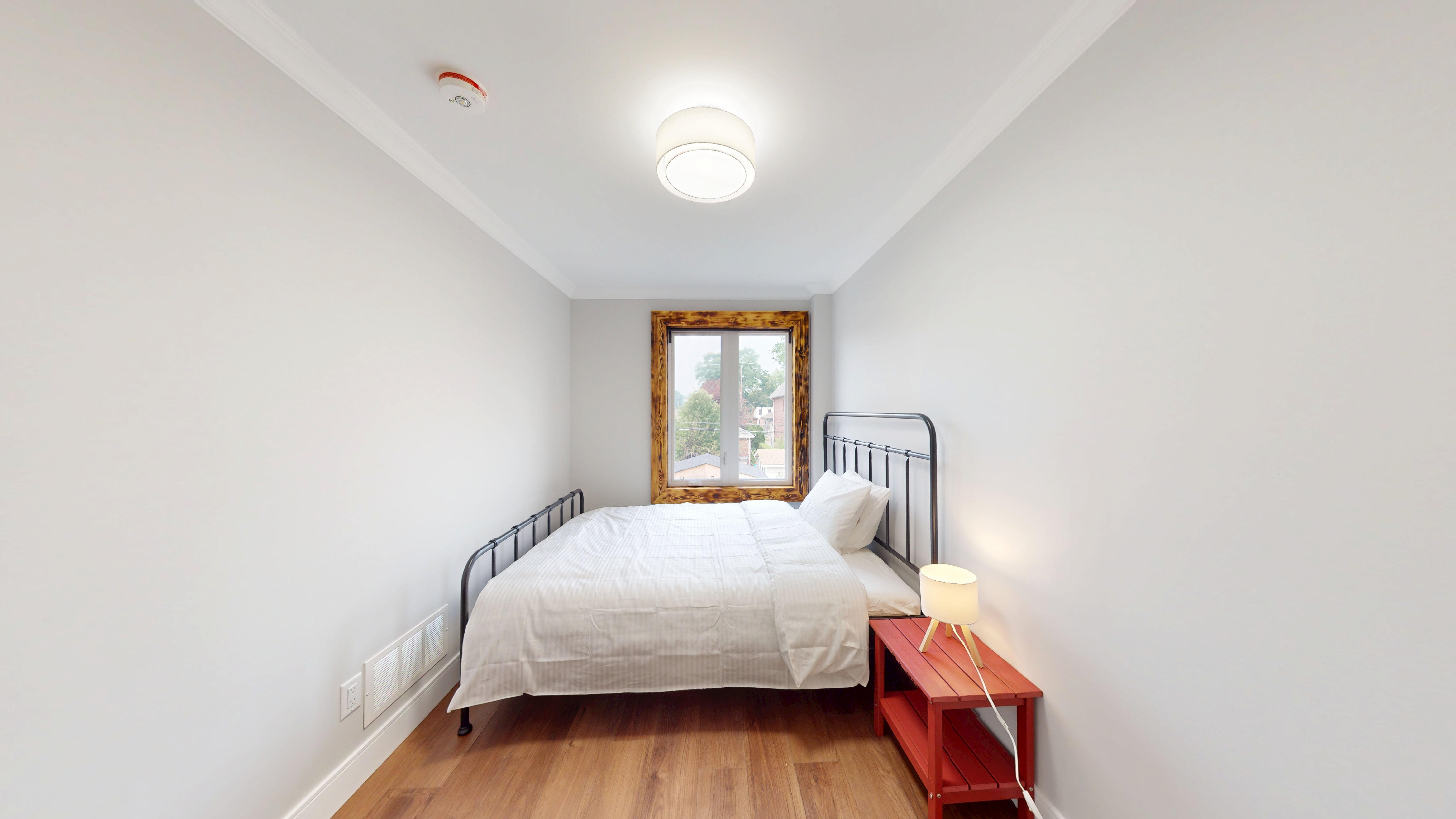 Bedroom with a red bedside bench beneath a burnt-wood framed window